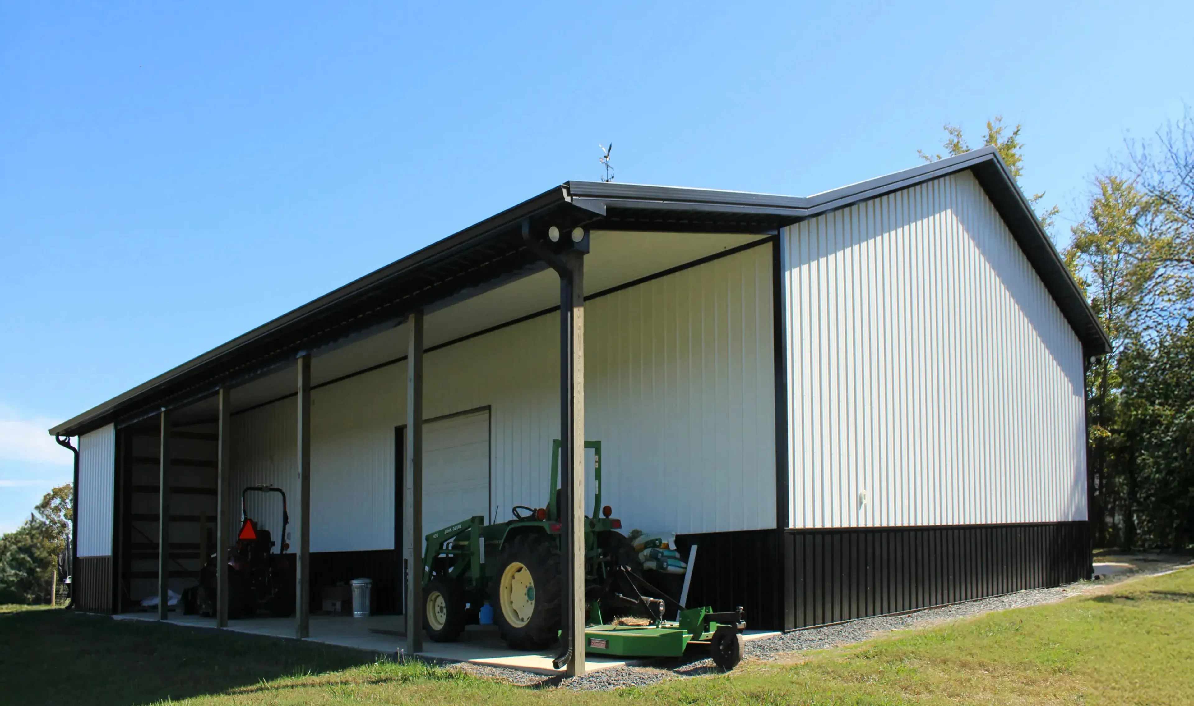 Large metal agricultural shed with open side housing a tractor and equipment on grassy land.