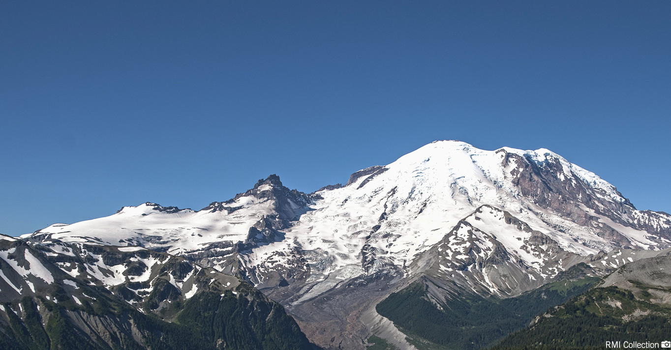 Snow-covered mountain peak with rugged terrain under a clear blue sky.