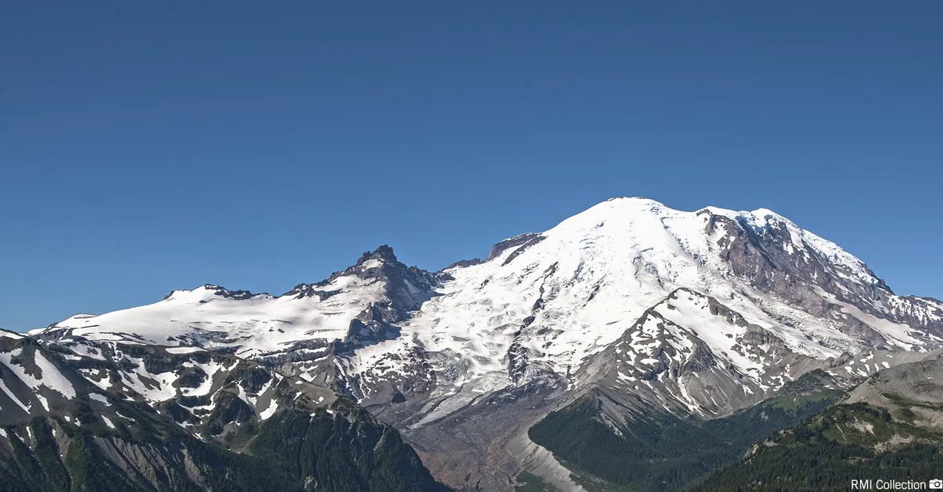 Snow-covered mountain peak with rugged terrain under a clear blue sky.