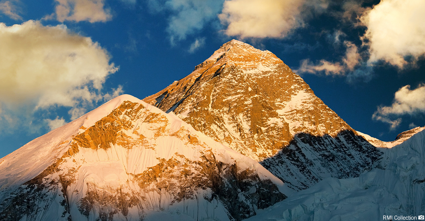 Sunlit snow-covered mountain peaks under a partly cloudy blue sky.