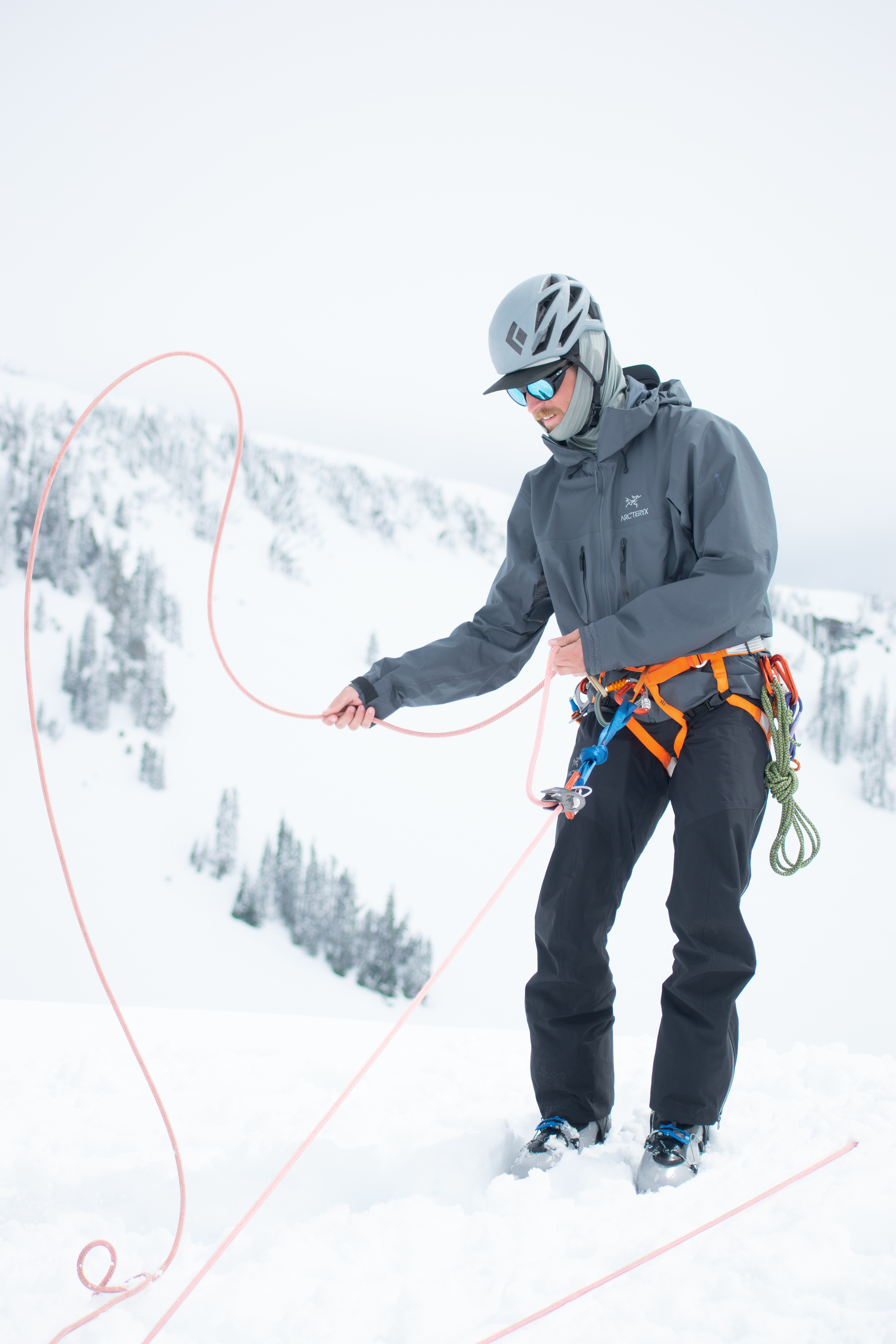 Person in helmet and climbing gear managing rope in snowy mountain landscape.