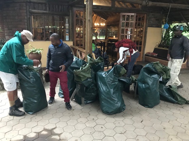 Four people packing and arranging large green bags outside a rustic building with wooden beams.