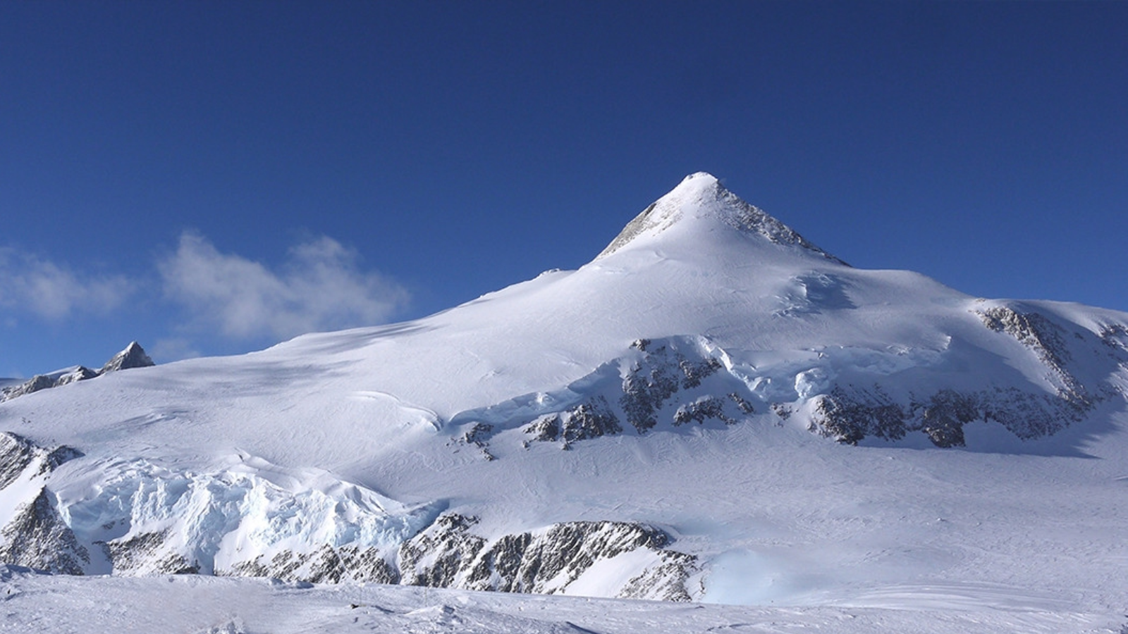 Snow-covered mountain peak under a clear blue sky with some clouds at the horizon.