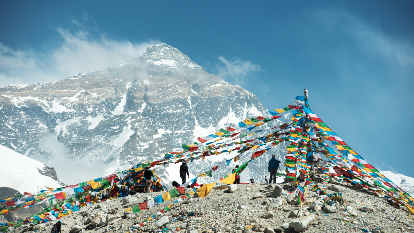 Colorful prayer flags on rocky ground with Mount Everest's snow-covered peak in the background.