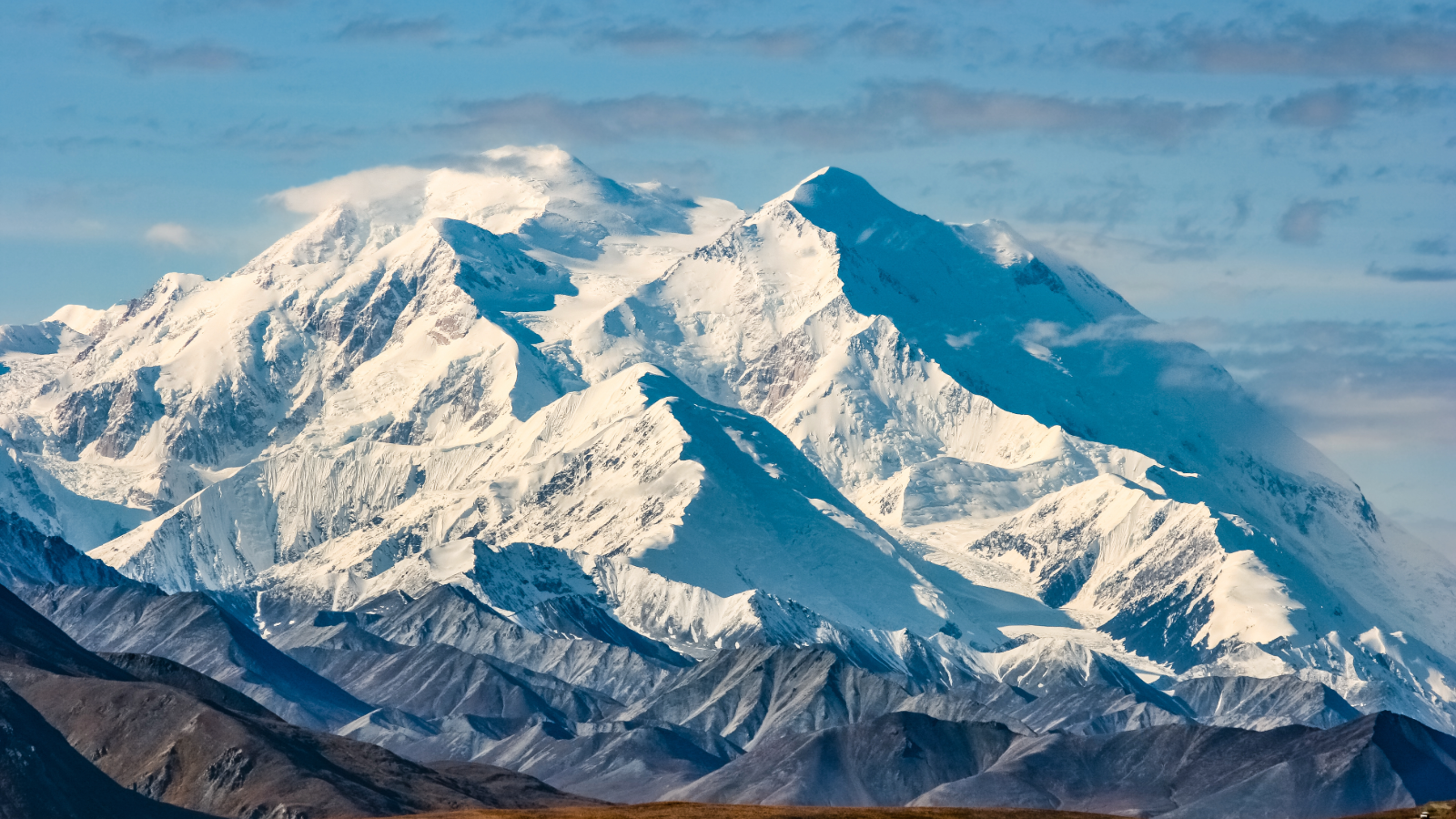 Snow-covered mountain peaks under a blue sky with scattered clouds at daylight.