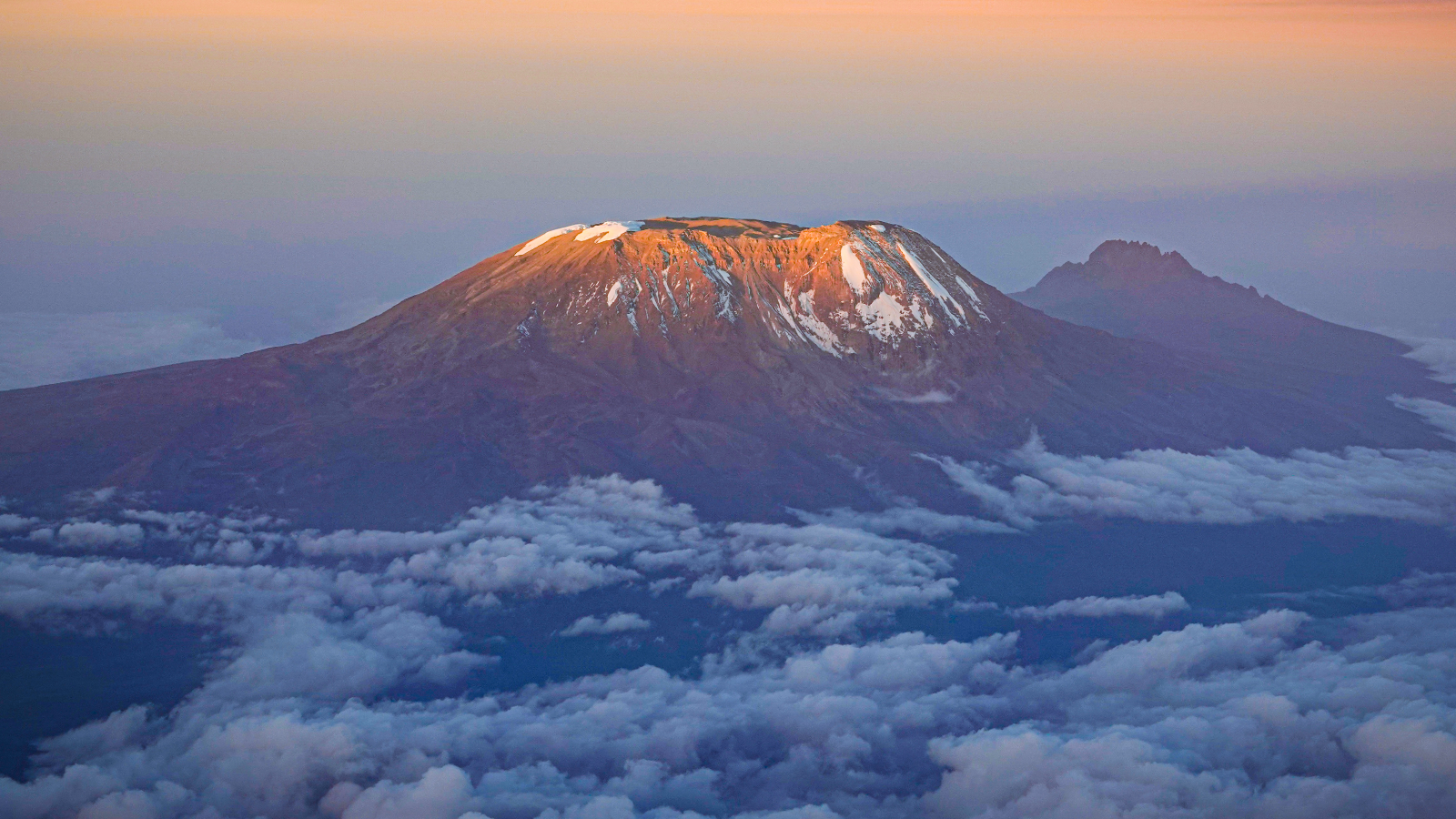 Mount Kilimanjaro at sunrise with snow patches above a sea of clouds.