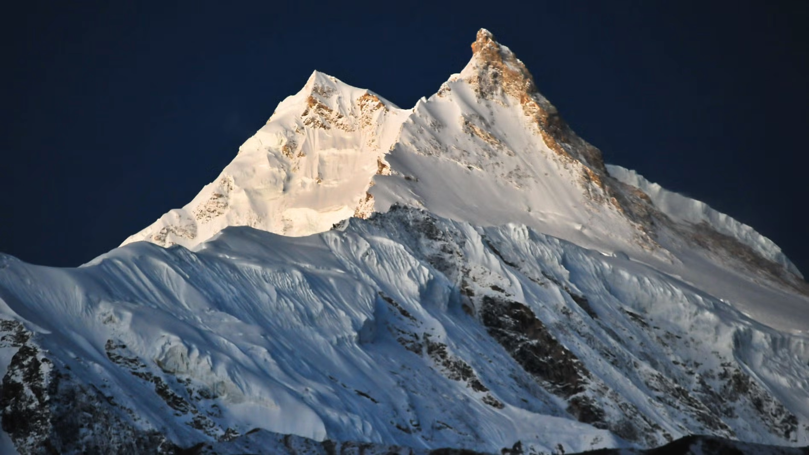 Snow-covered mountain peaks illuminated against a dark sky.