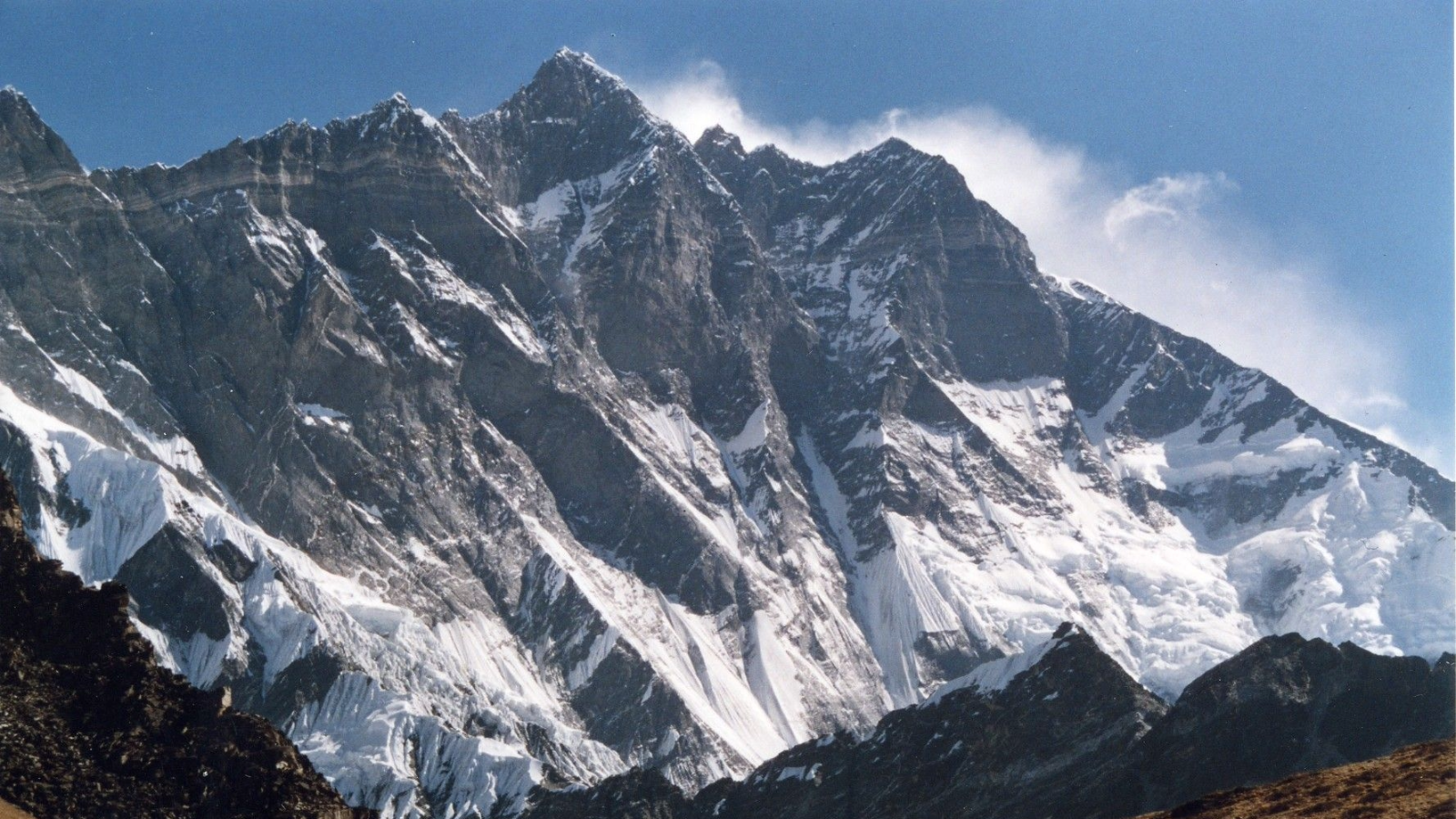 Snow-covered rugged mountain peaks under a clear blue sky with dark rocky foreground ridges.