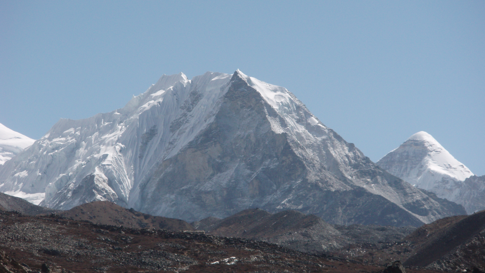 Snow-capped rocky mountain peaks under clear blue sky with rugged terrain in foreground.