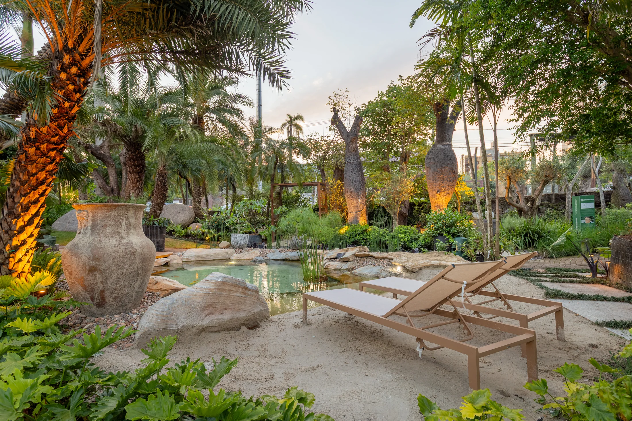 Two lounge chairs next to a small pond with tropical plants and large stone pots around.