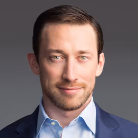 Headshot of a man with light skin, short brown hair, blue eyes, wearing a blue suit and light blue shirt.