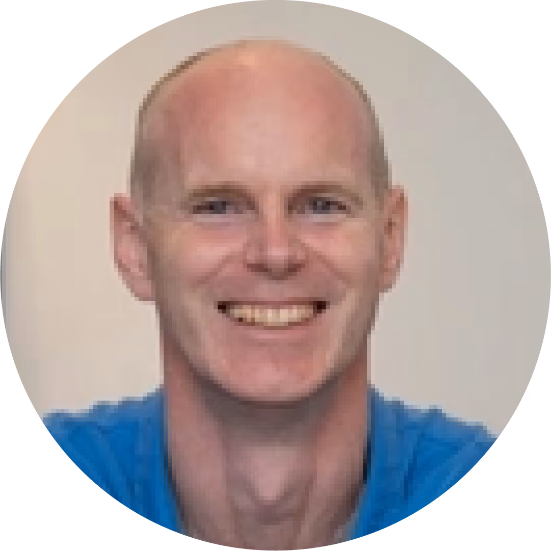 Smiling bald man wearing a blue shirt in a circular frame with a plain background.