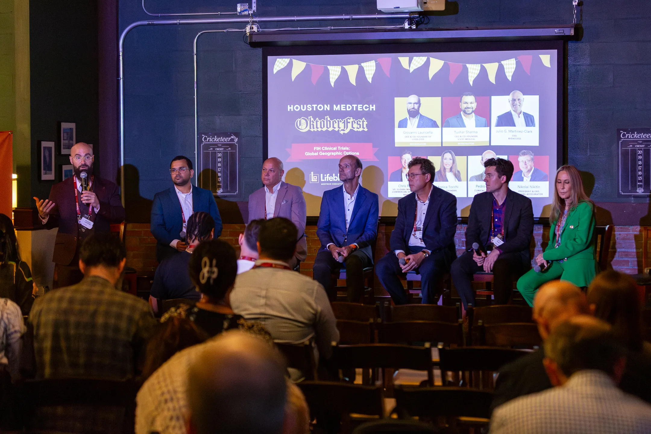 Panel of eight professionals seated and speaking with audience at Houston MedTech Oktoberfest event.