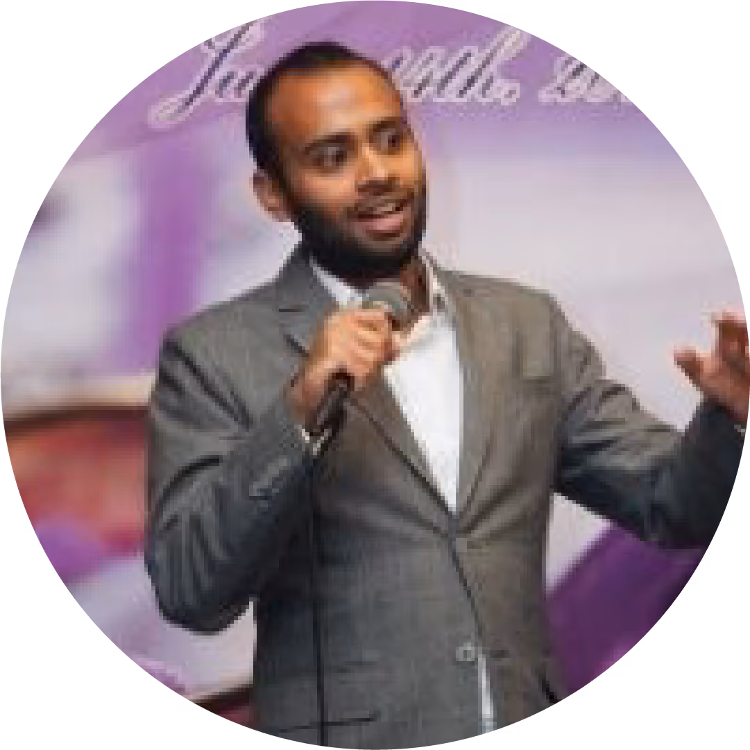 Man in gray suit speaking into a microphone with a purple background.