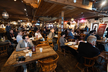 A diverse group of people seated indoors attentively listening and drinking coffee at a conference or meeting.