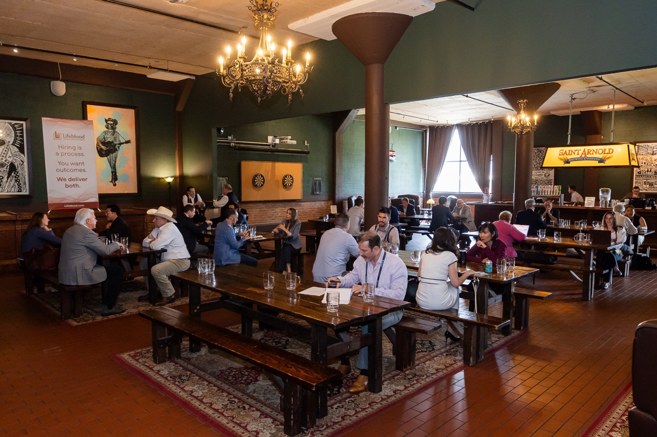 A group of people networking in a dimly lit room with colorful decor and statues.