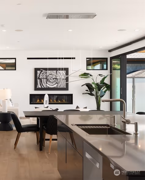 Modern two-story house exterior with concrete driveway, wooden front door, two black chairs with yellow cushions on the porch, and green lawn.
