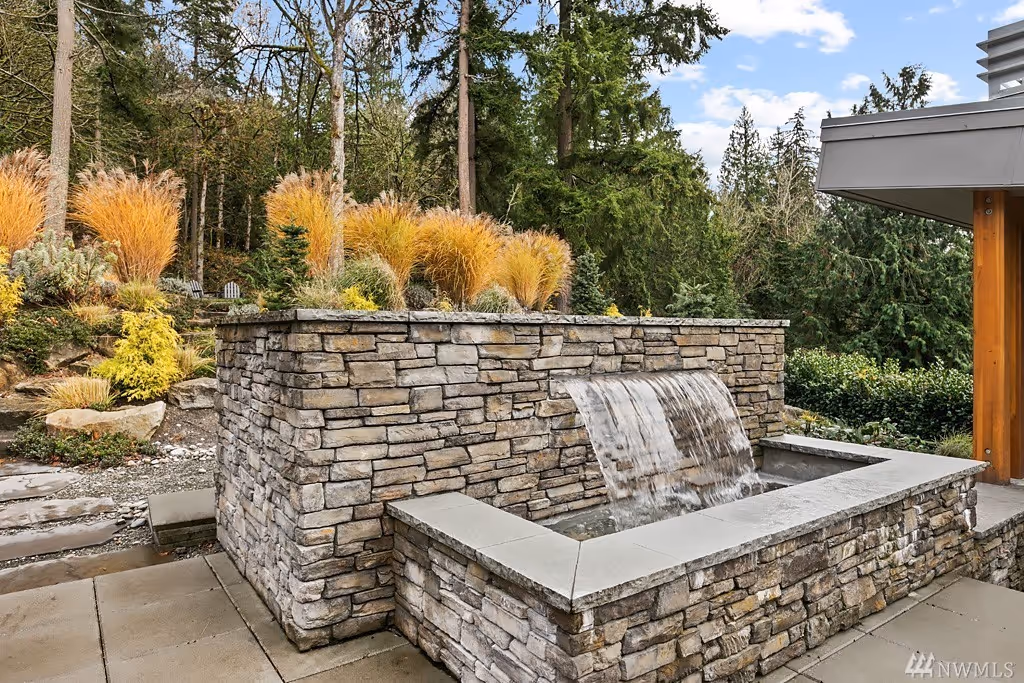 Modern white kitchen island with a bowl of bananas and oranges, gas stove, and a background of plants, stairs, and living area.