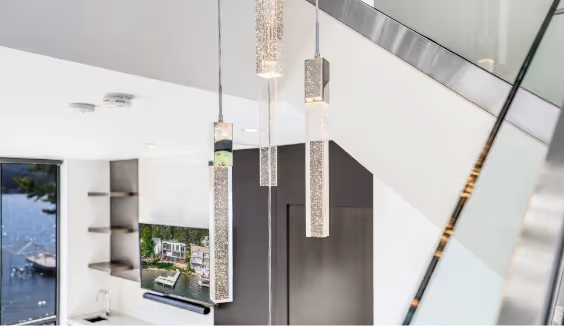 Modern interior with three hanging rectangular pendant lights and a wall-mounted TV showing a lakeside house scene.