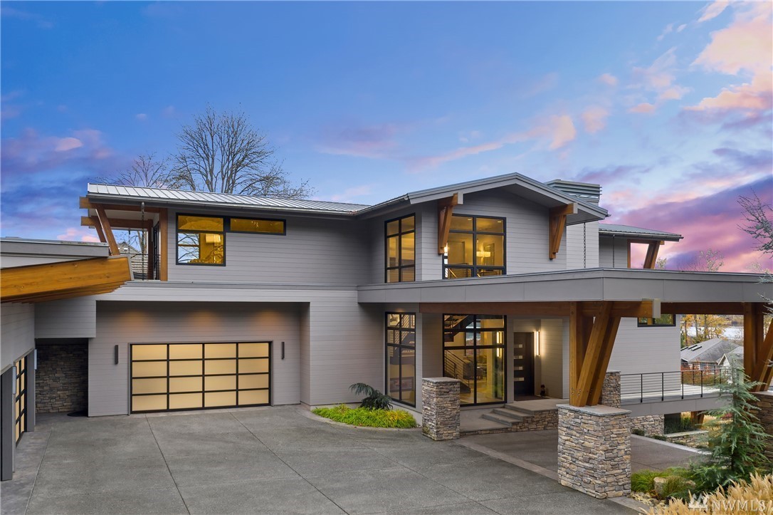 Modern two-story house with large windows, stone pillars, and a spacious driveway under a blue and purple evening sky.