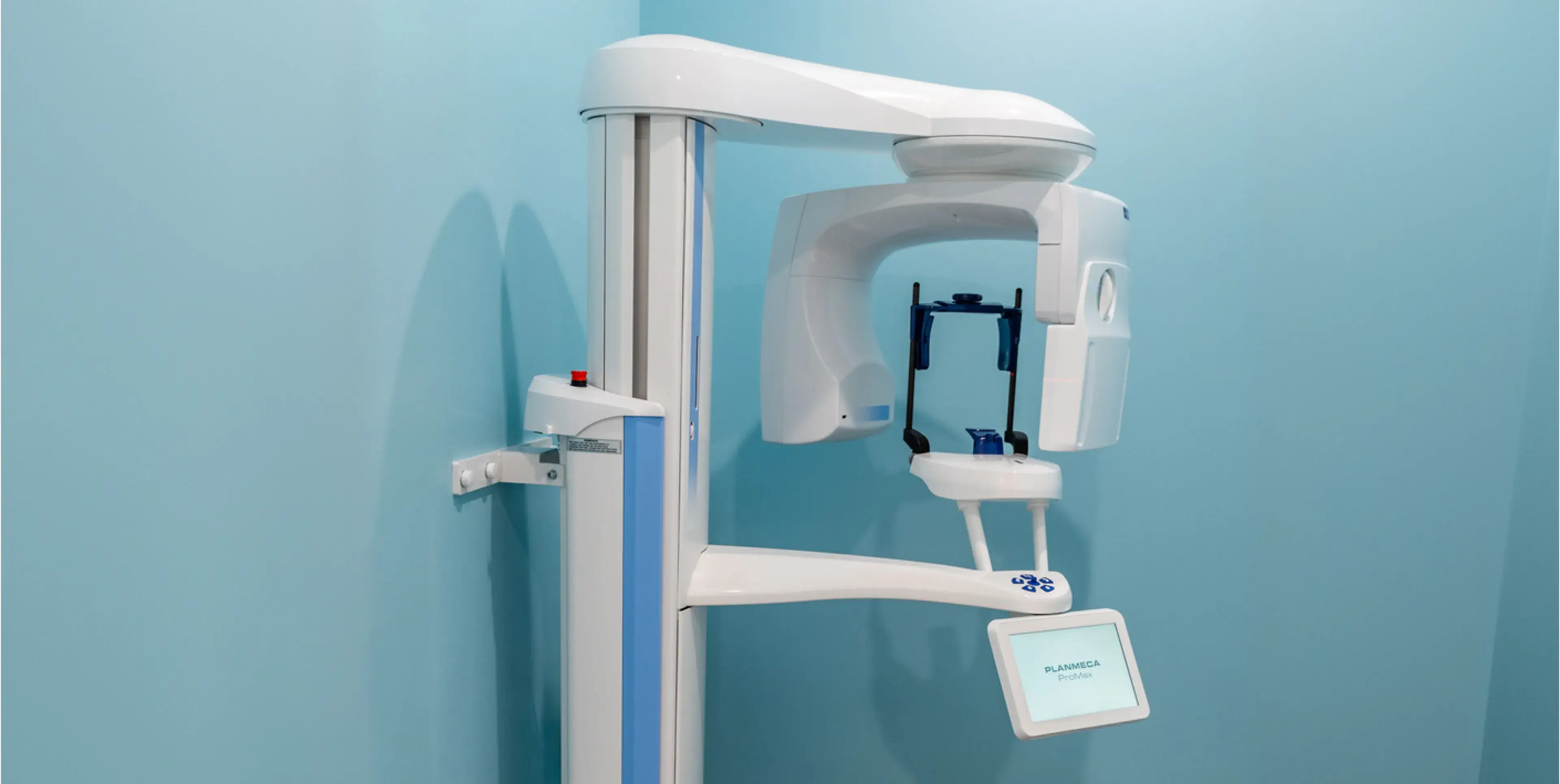 Planmeca ProMax dental X-ray machine mounted on a light blue wall in a clinic.