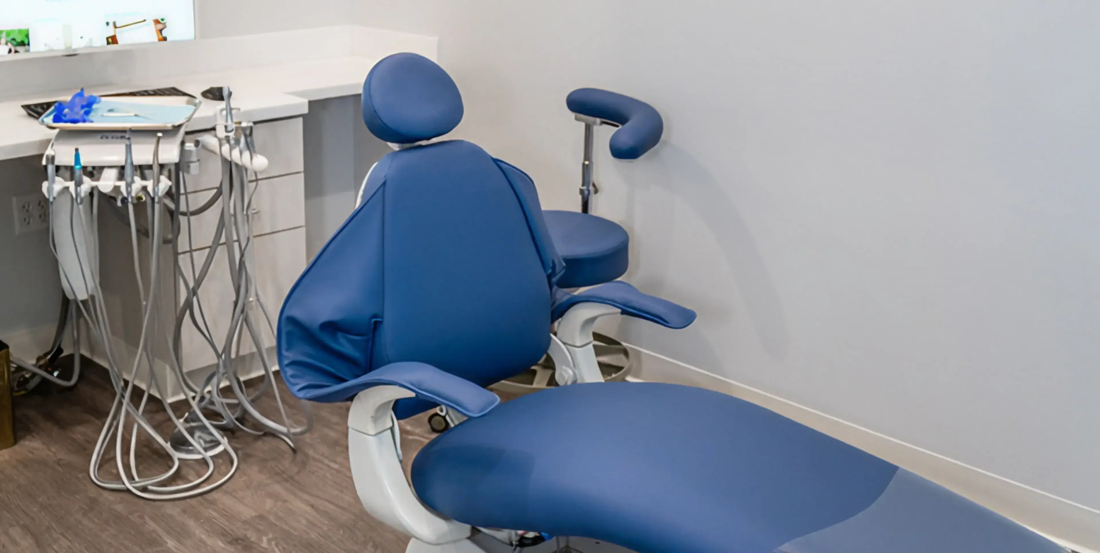 Blue padded dental chair with attached dental instruments and a matching blue stool in a dental clinic room.