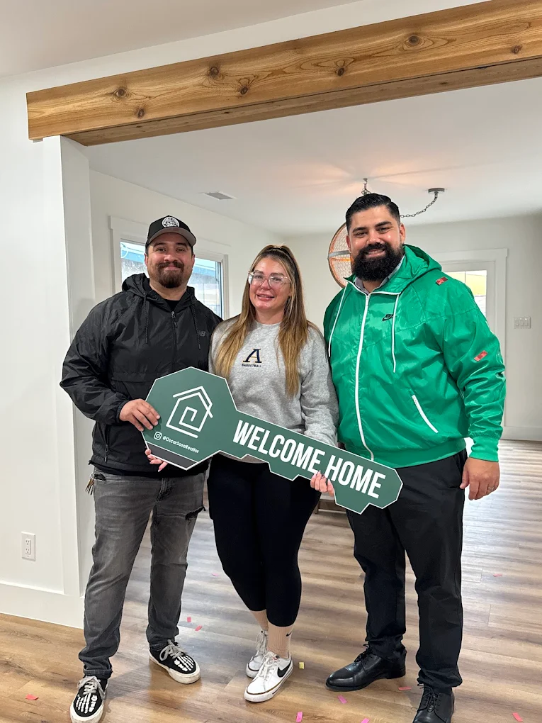 Two people indoors holding and swinging bright pink foam batons playfully on a wood floor with white walls and exposed wooden ceiling beam.