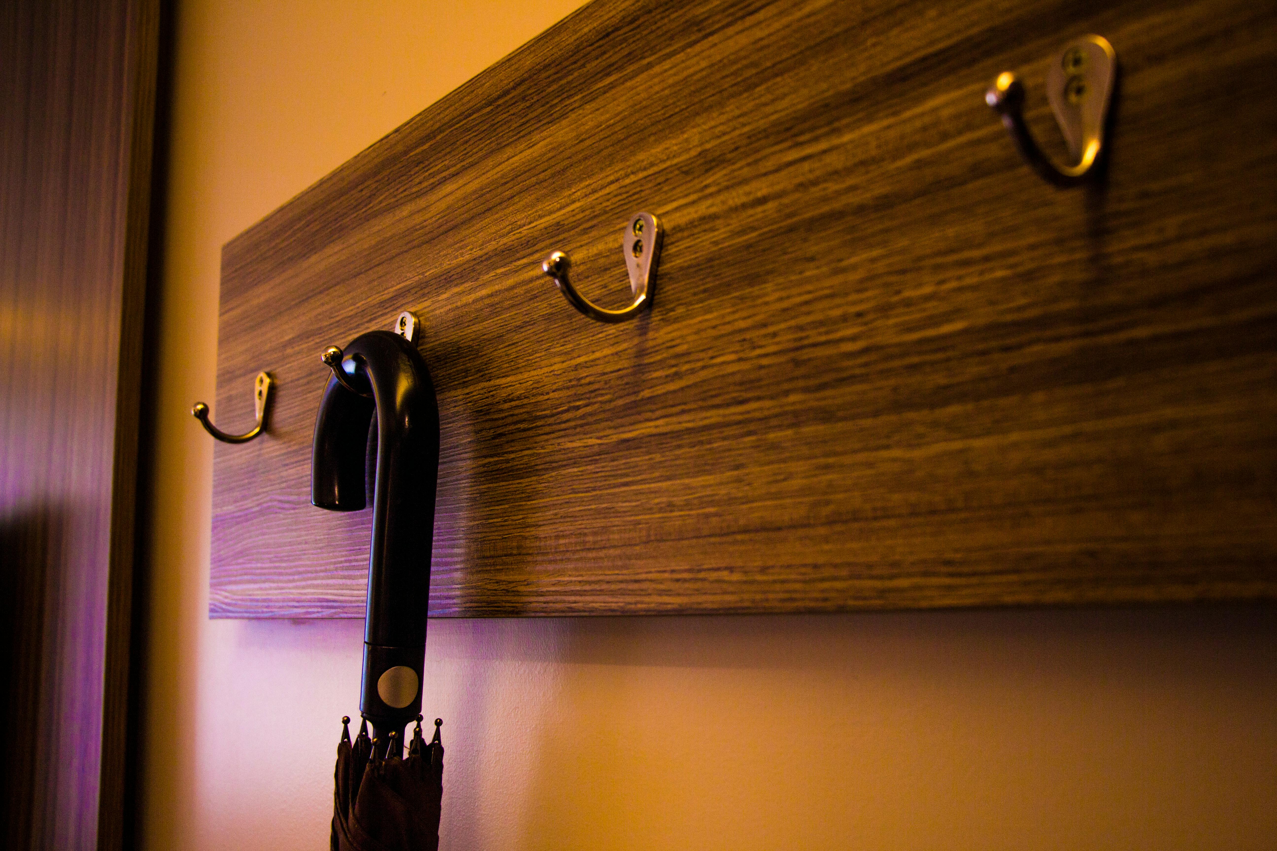 Wood wall-mounted coat rack with metal hooks and a folded umbrella hanging against a light-colored wall under warm lighting.