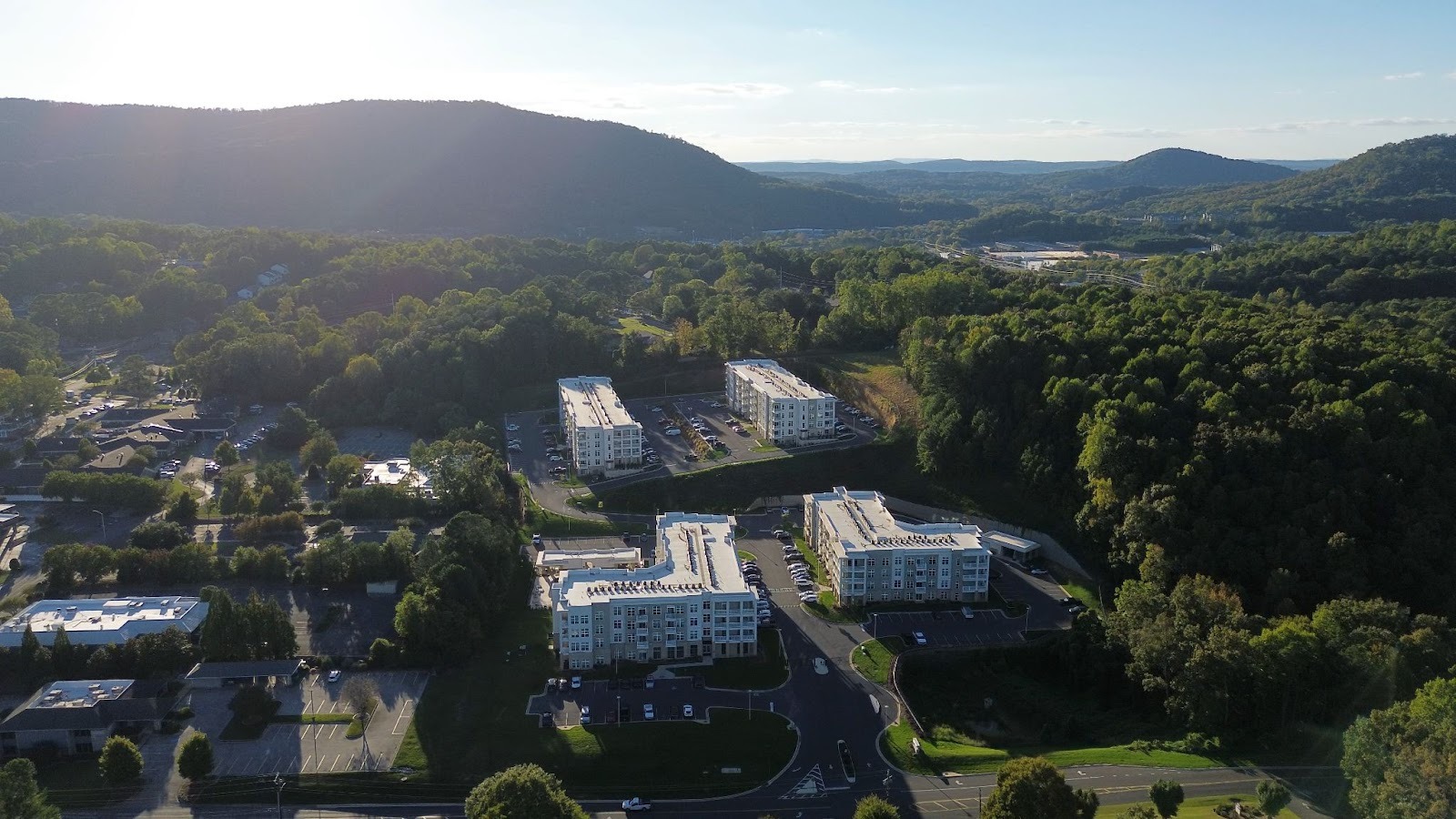A drone shot of modern apartment buildings featuring white exteriors and flat roofs sitting nestled in a green valley.