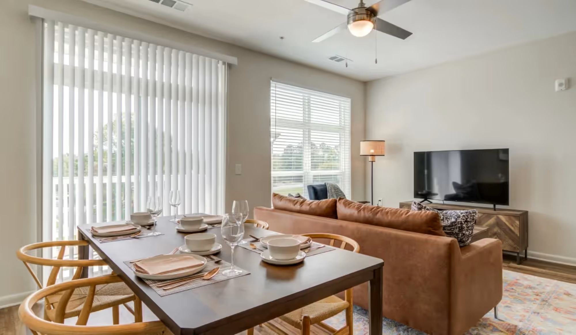 An open living area featuring a dark wooden dining table set with place settings alongside a brown leather sofa.