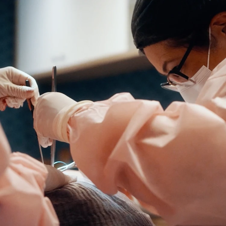 Médico usando máscara, óculos e jaleco rosa realizando procedimento cirúrgico com instrumentos médicos. (material para empresa Dra Priscila Oshiro)