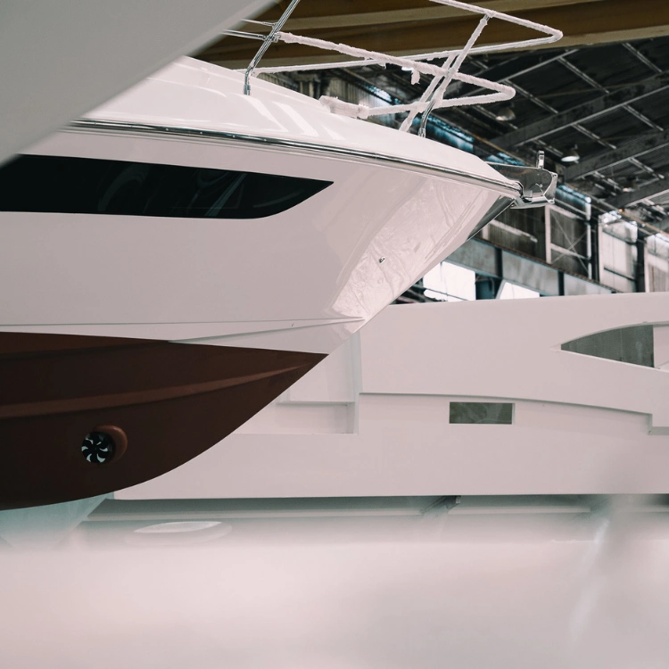 Homem trabalhando na estrutura branca de um iate em um grande galpão industrial.(material para empresa Intermarine)