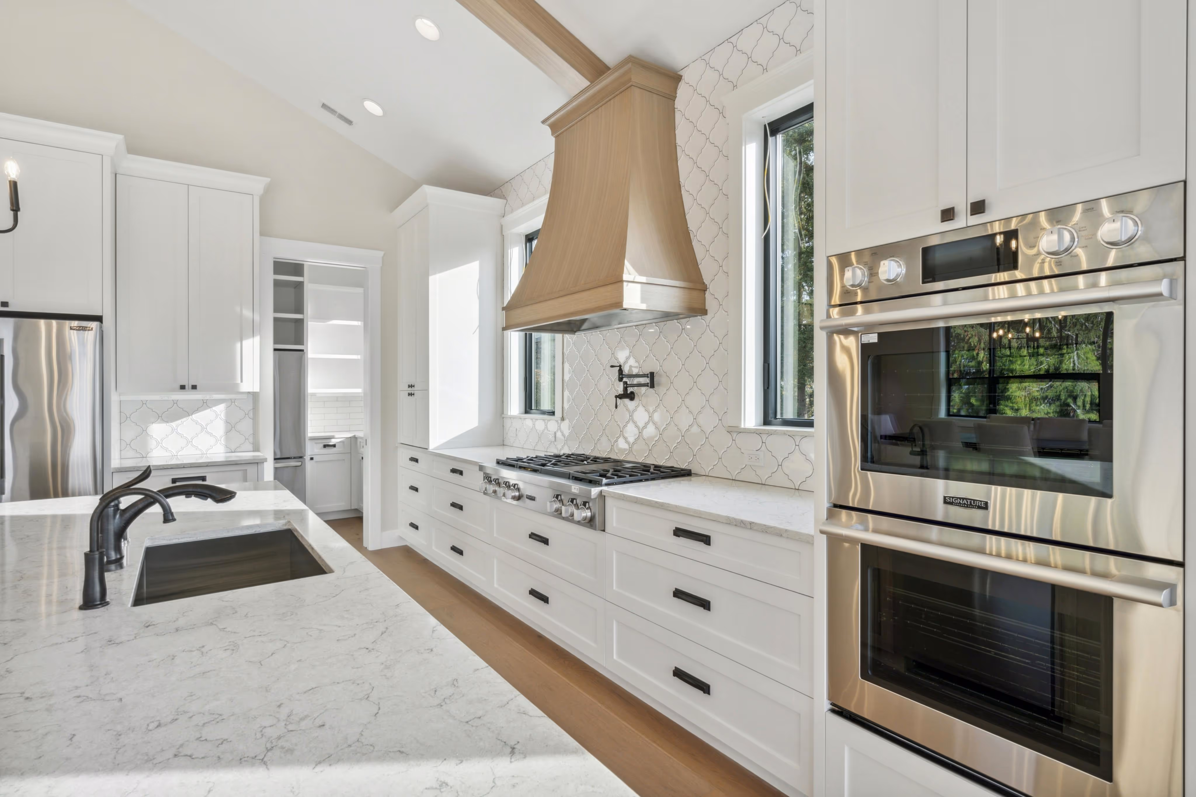 Modern open-concept living room and kitchen with light wood cabinetry, white sofa, bar stools, and a large green landscape painting.