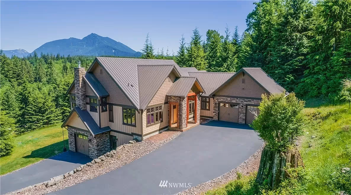 Modern open-concept living room and kitchen with light wood cabinetry, white sofa, bar stools, and a large green landscape painting.