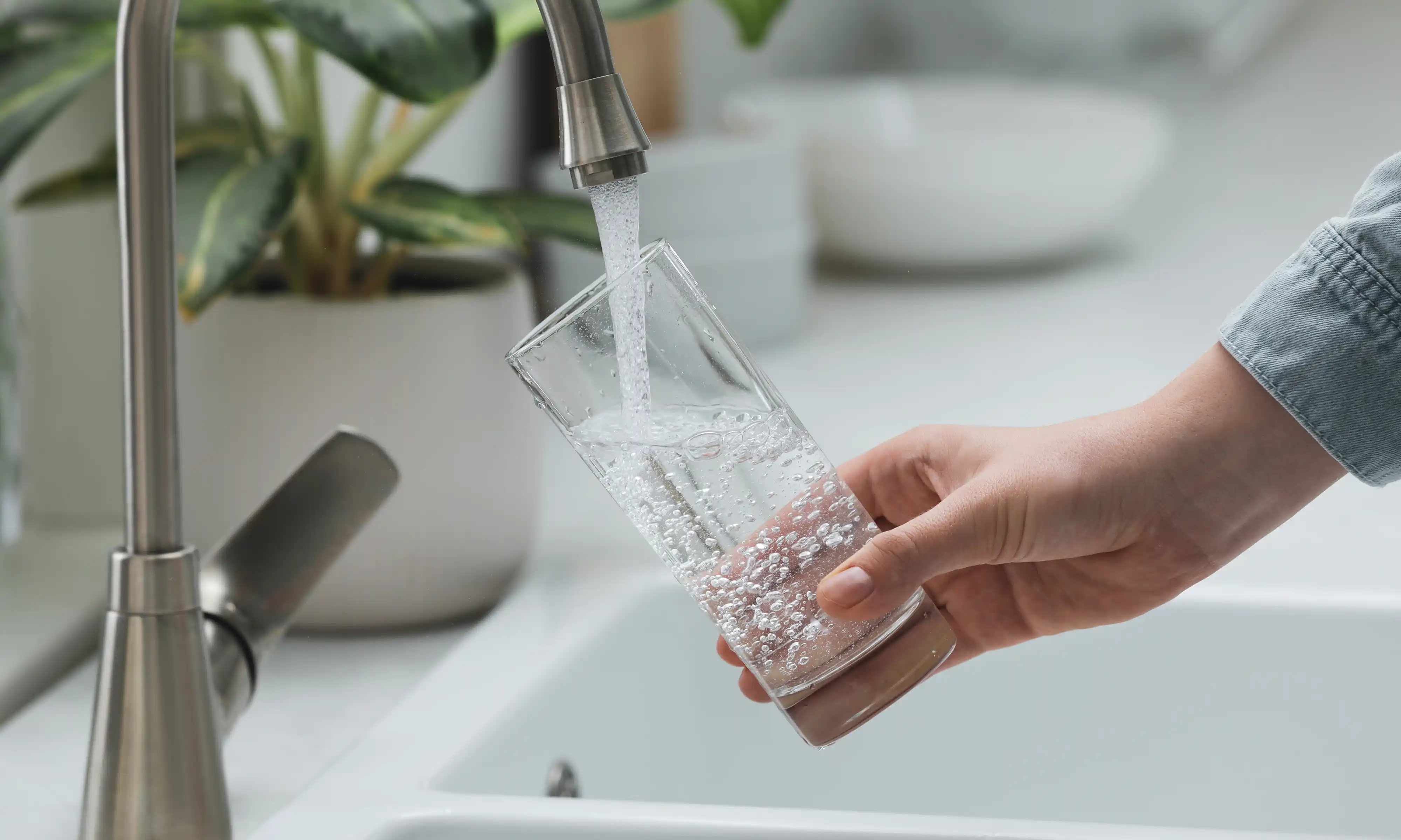 Hand holding a clear glass under a kitchen faucet filling it with water.