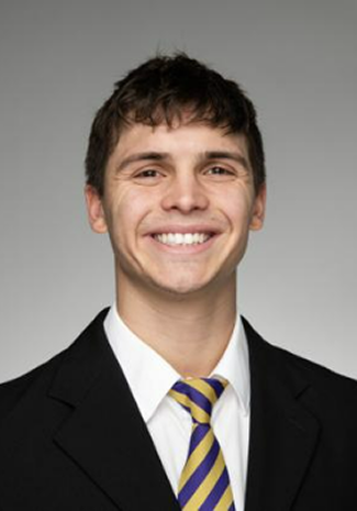 Smiling young man with short brown hair wearing a black suit, white shirt, and yellow and purple striped tie.