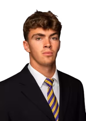 Young man with curly brown hair wearing a black suit, white shirt, and purple and yellow striped tie.