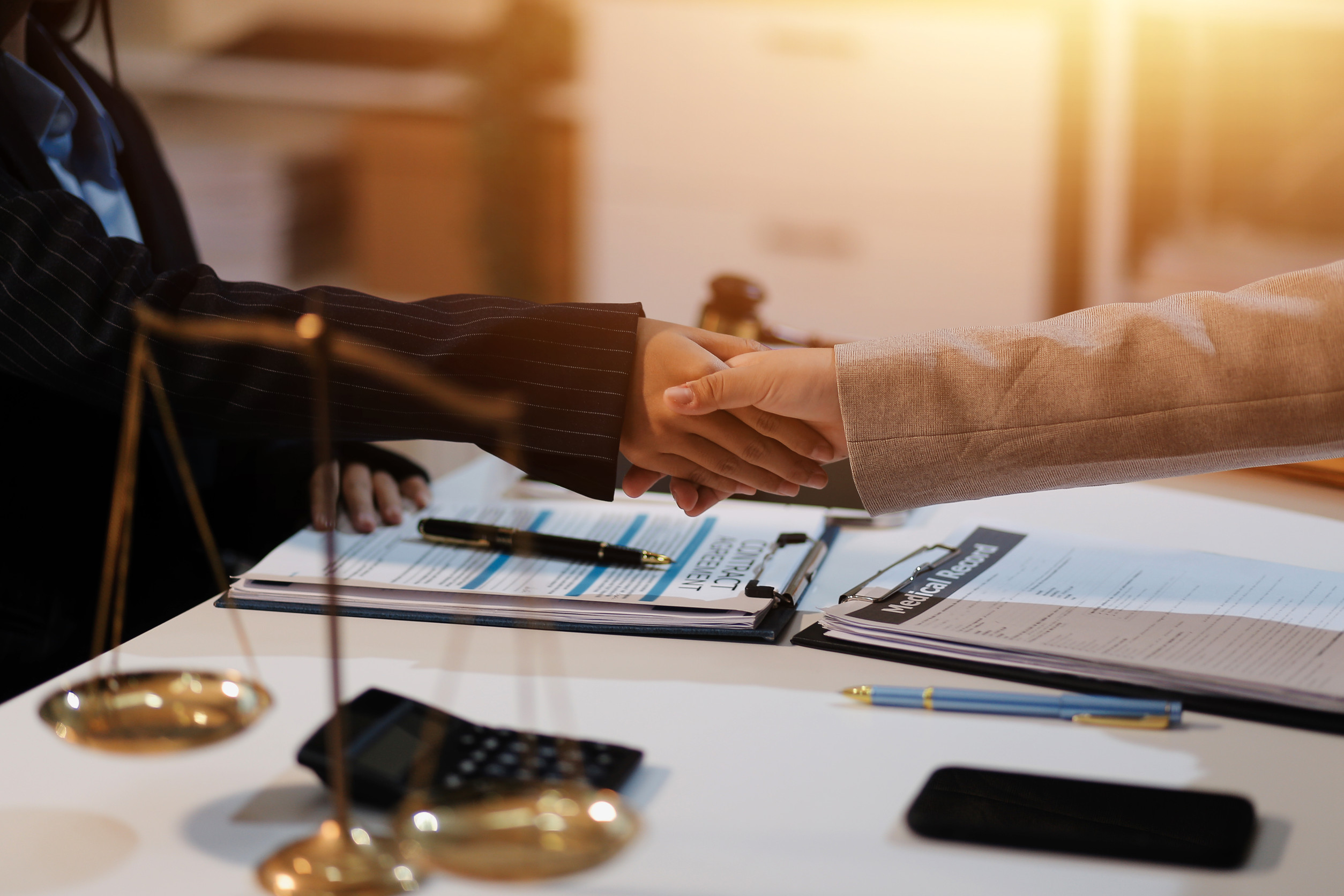 Two professionals shaking hands over a desk with contract and law records