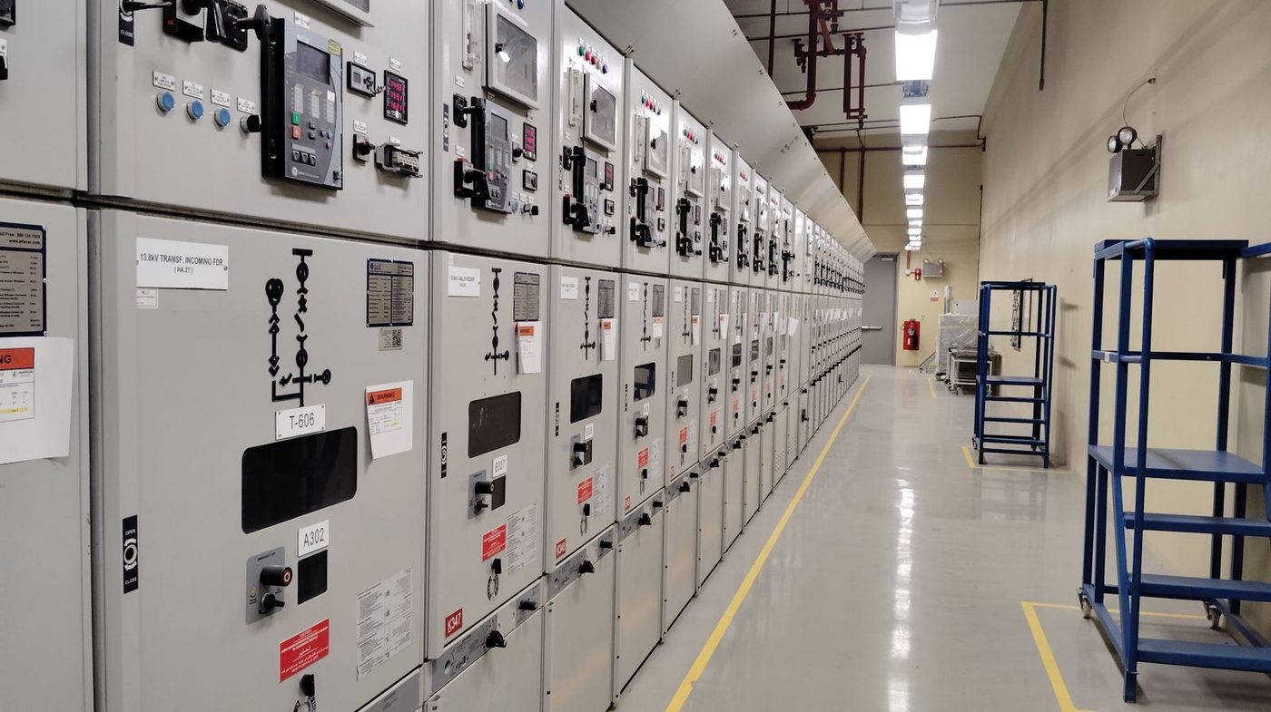 Row of medium-voltage electrical switchgear panels lining a plant power distribution room