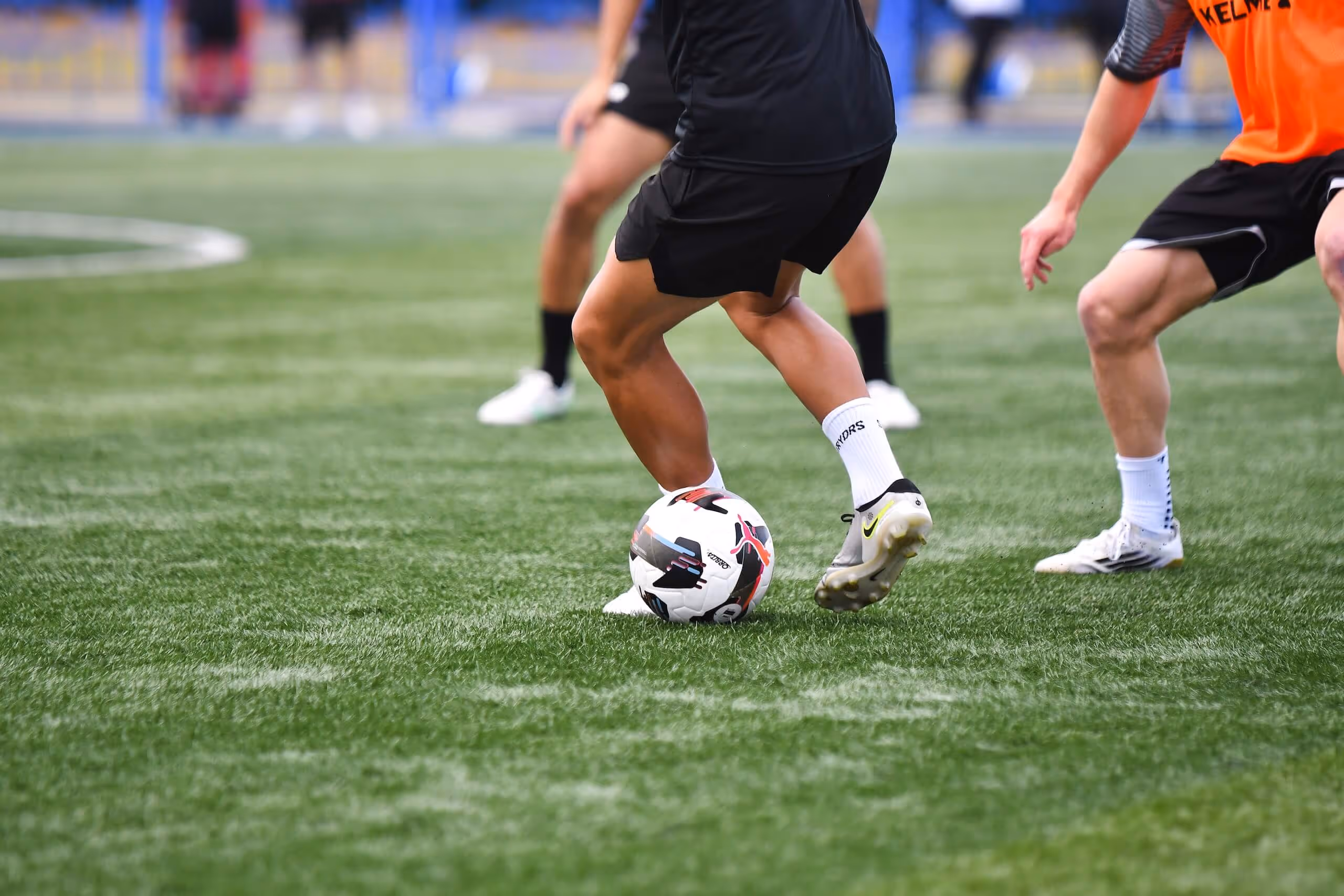 Close-up of soccer players' legs in action on a green field, with one player controlling a soccer ball.
