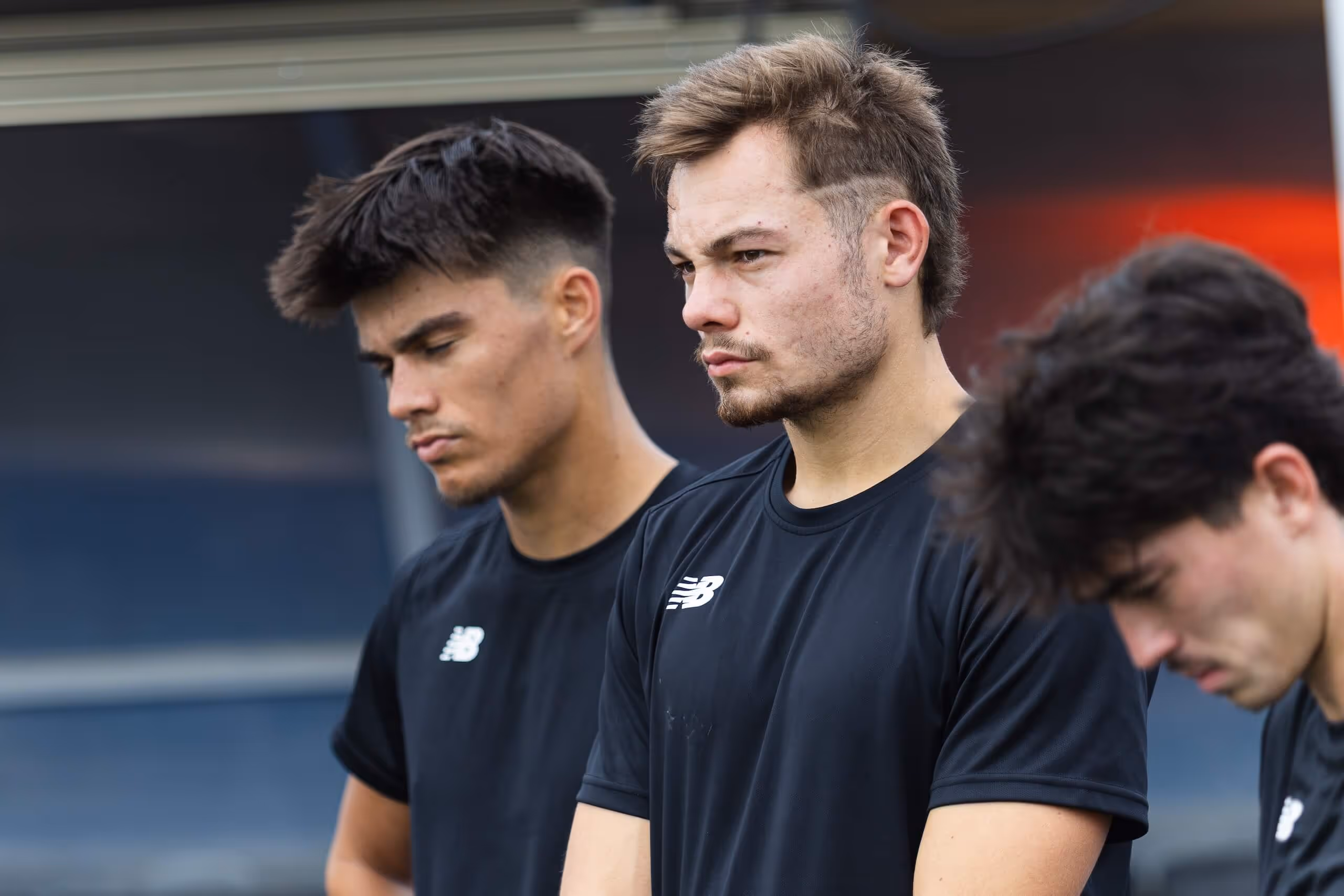Three young men in black sports shirts standing closely with serious and contemplative expressions.