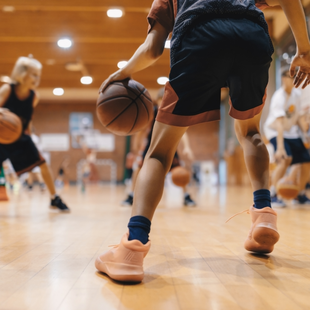 Close-up of a basketball player dribbling the ball on an indoor court during practice with other players in the background.
