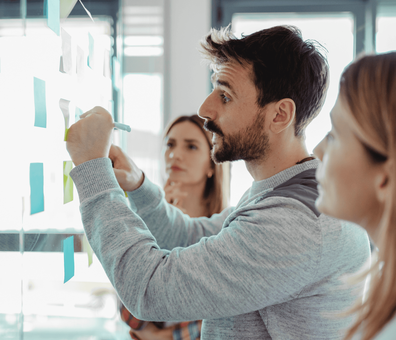 Three cybersecurity professionals, one man and two women, working through a security issue by posting sticky notes on a glass wall. Representative of the TPG Consulting website's homepage.