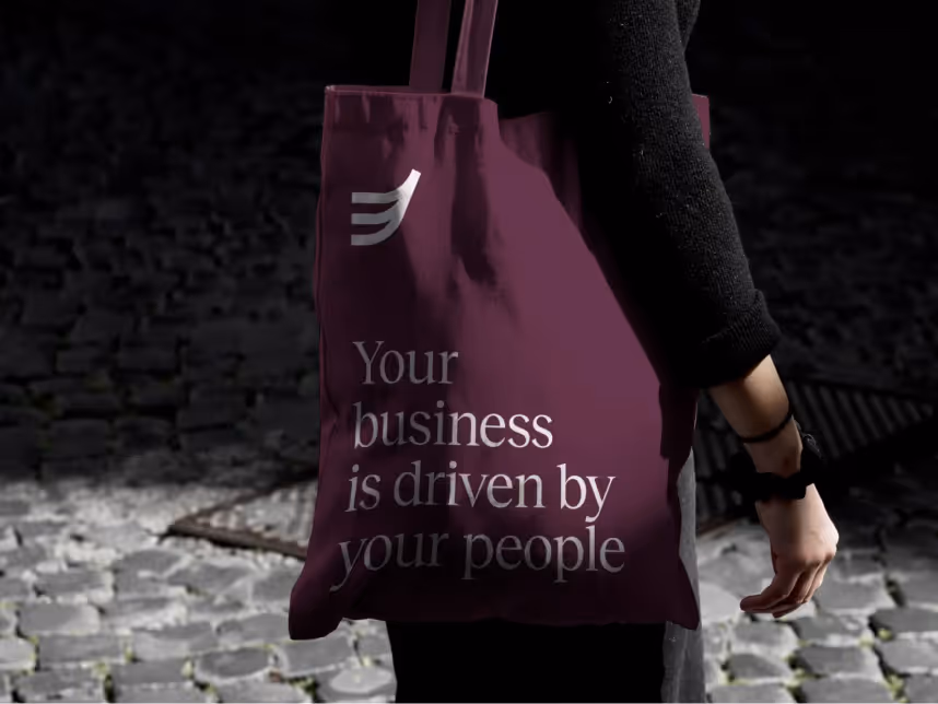 Person holding a purple tote bag with the text 'Your business is driven by your people' on a cobblestone street.