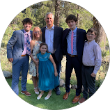 Group of two adult men and four children standing outdoors on grass with trees in the background, all dressed in formal attire.