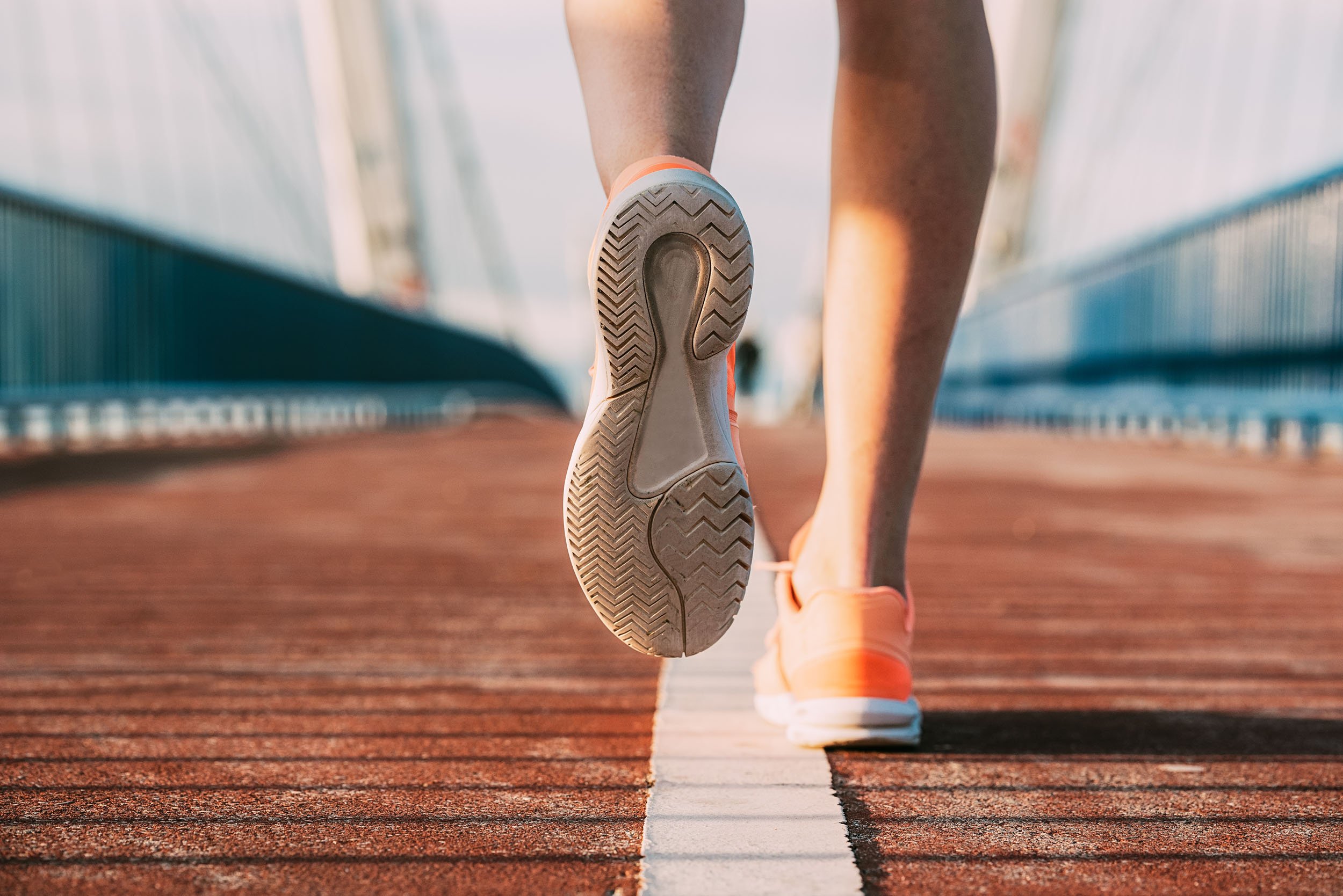 Close-up of a person walking on a track wearing orange running shoes, focusing on the sole of one shoe.