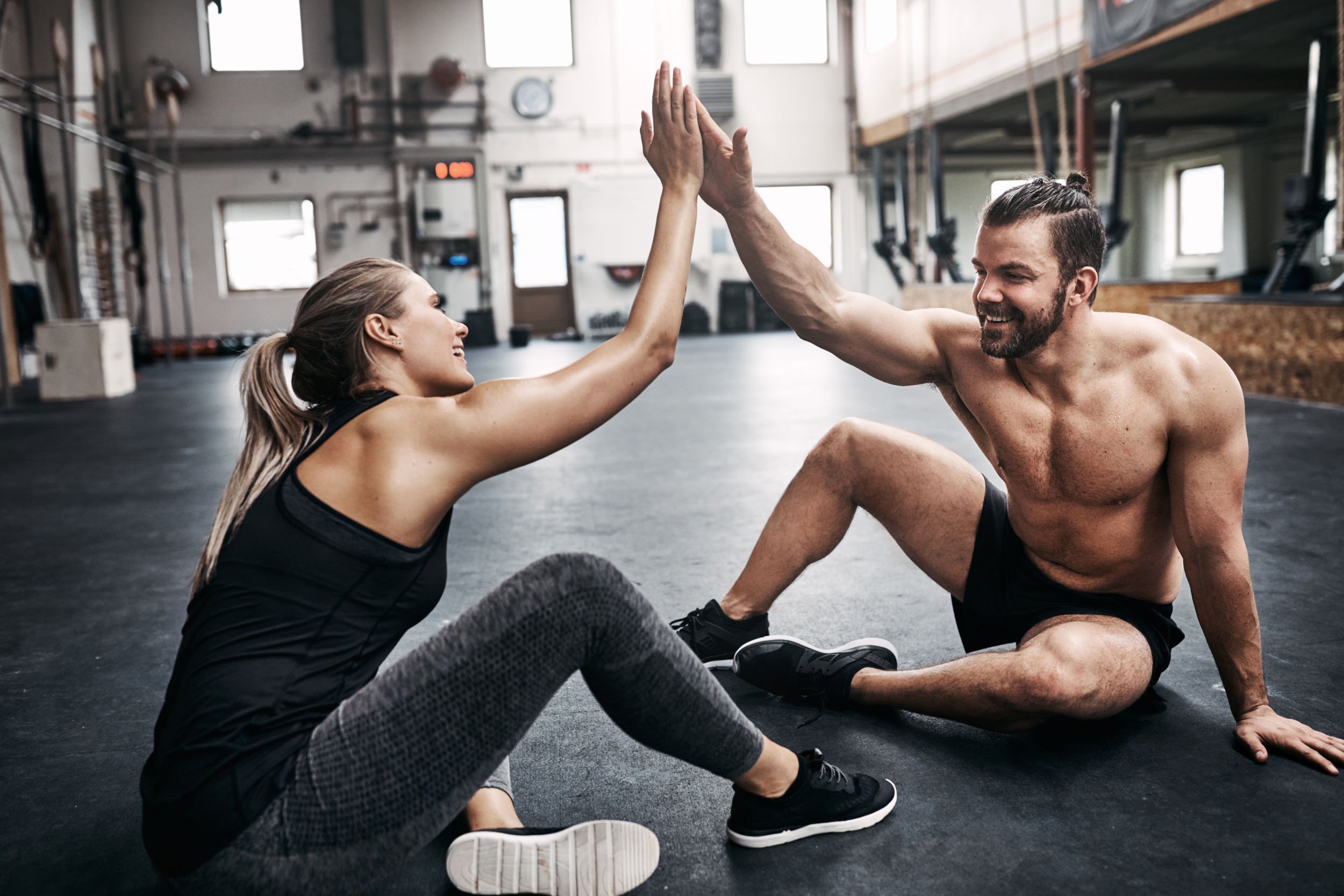 Smiling man and woman sitting on gym floor giving each other a high five.