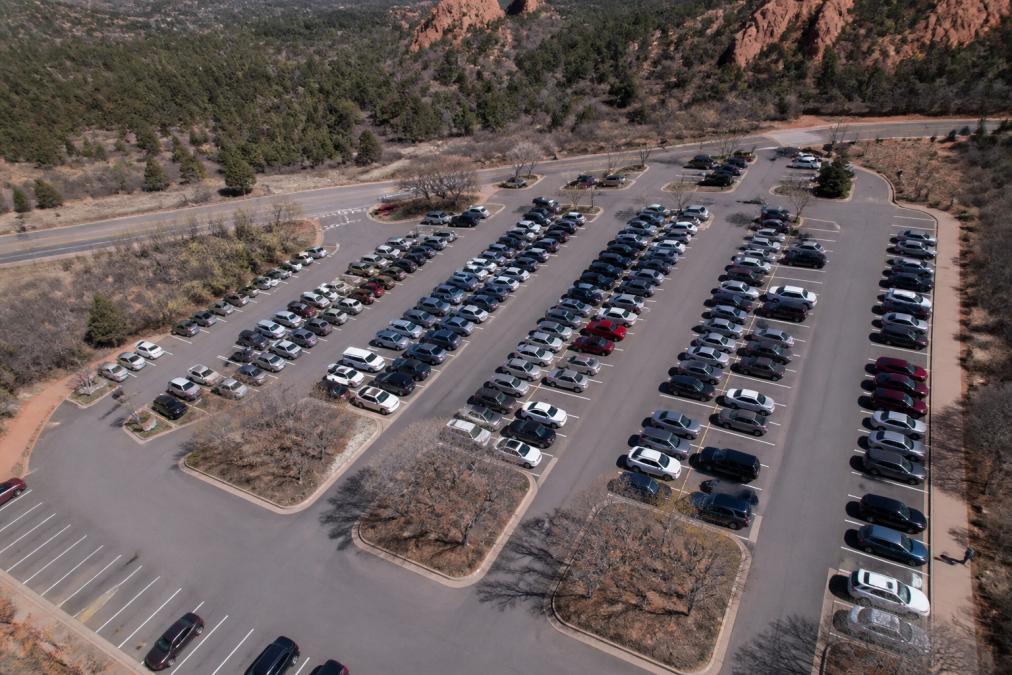 Aerial view of a parking lot during peak hours with multiple vehicles parked in organized rows, showing capacity usage with some empty spaces still visible among filled sections