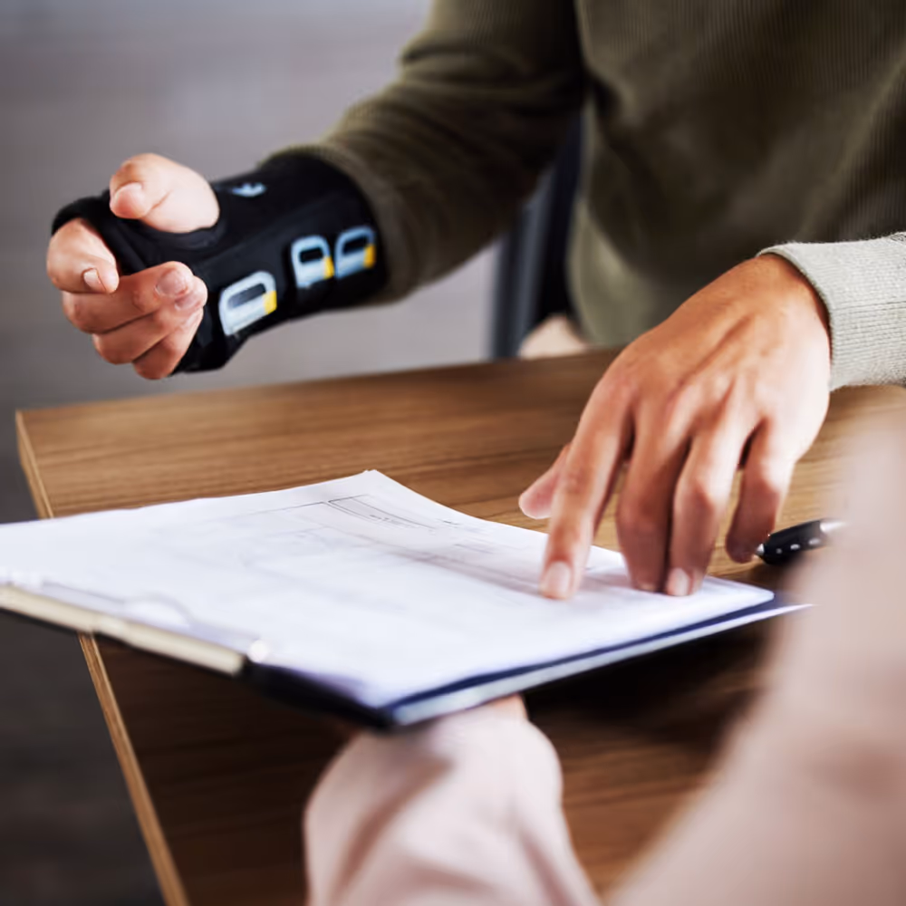 Person wearing a wrist brace pointing at a document on a clipboard during a consultation.