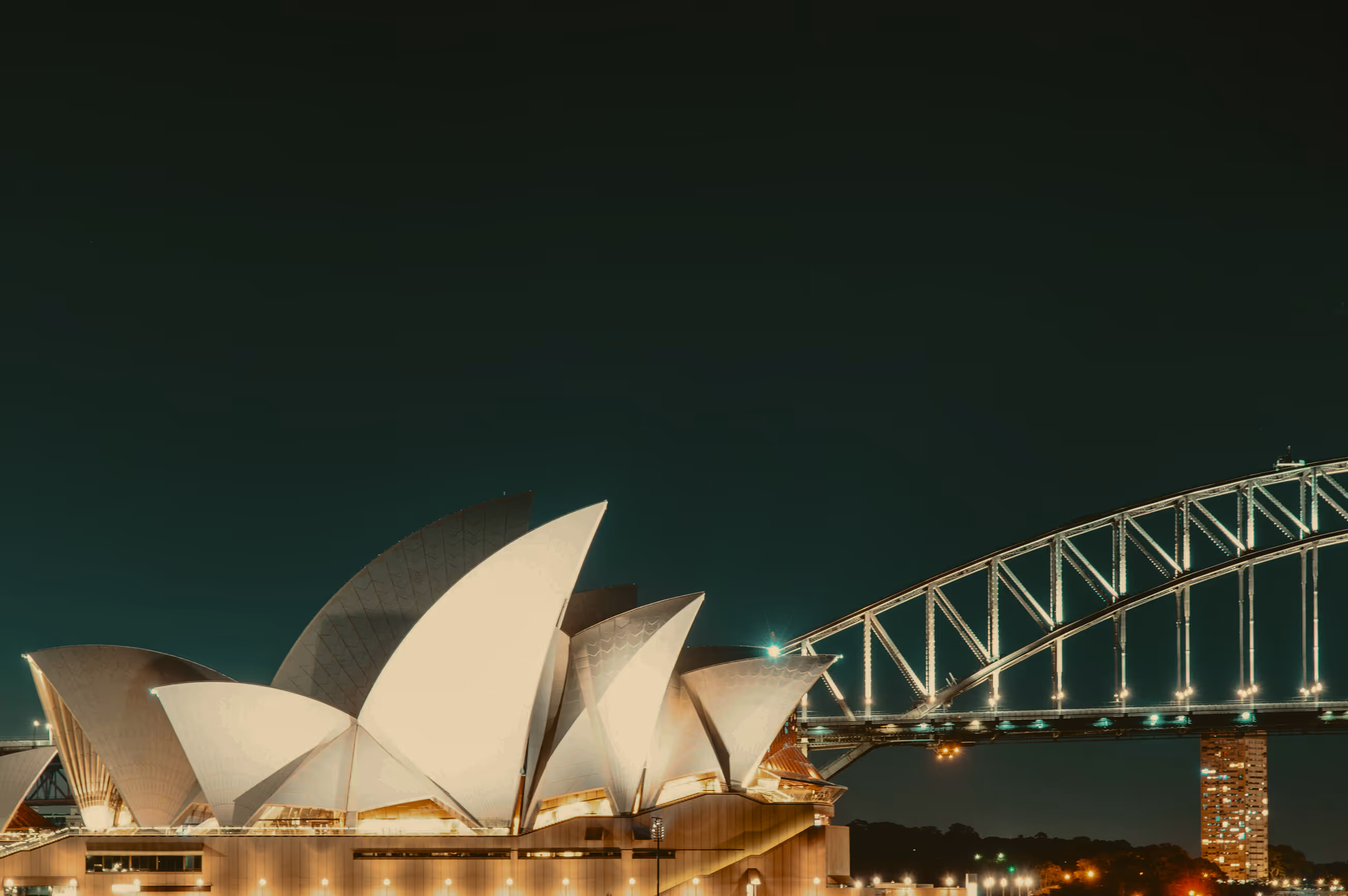 Sydney Opera House illuminated at night with Sydney Harbour Bridge in the background.